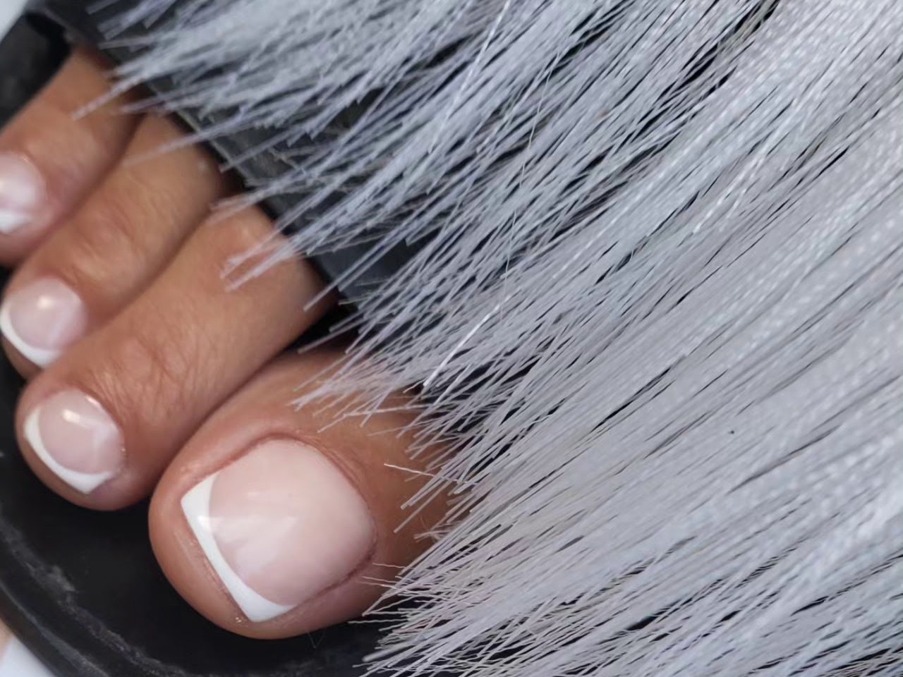 Pedicure met French teennagels naast een grijze vacht