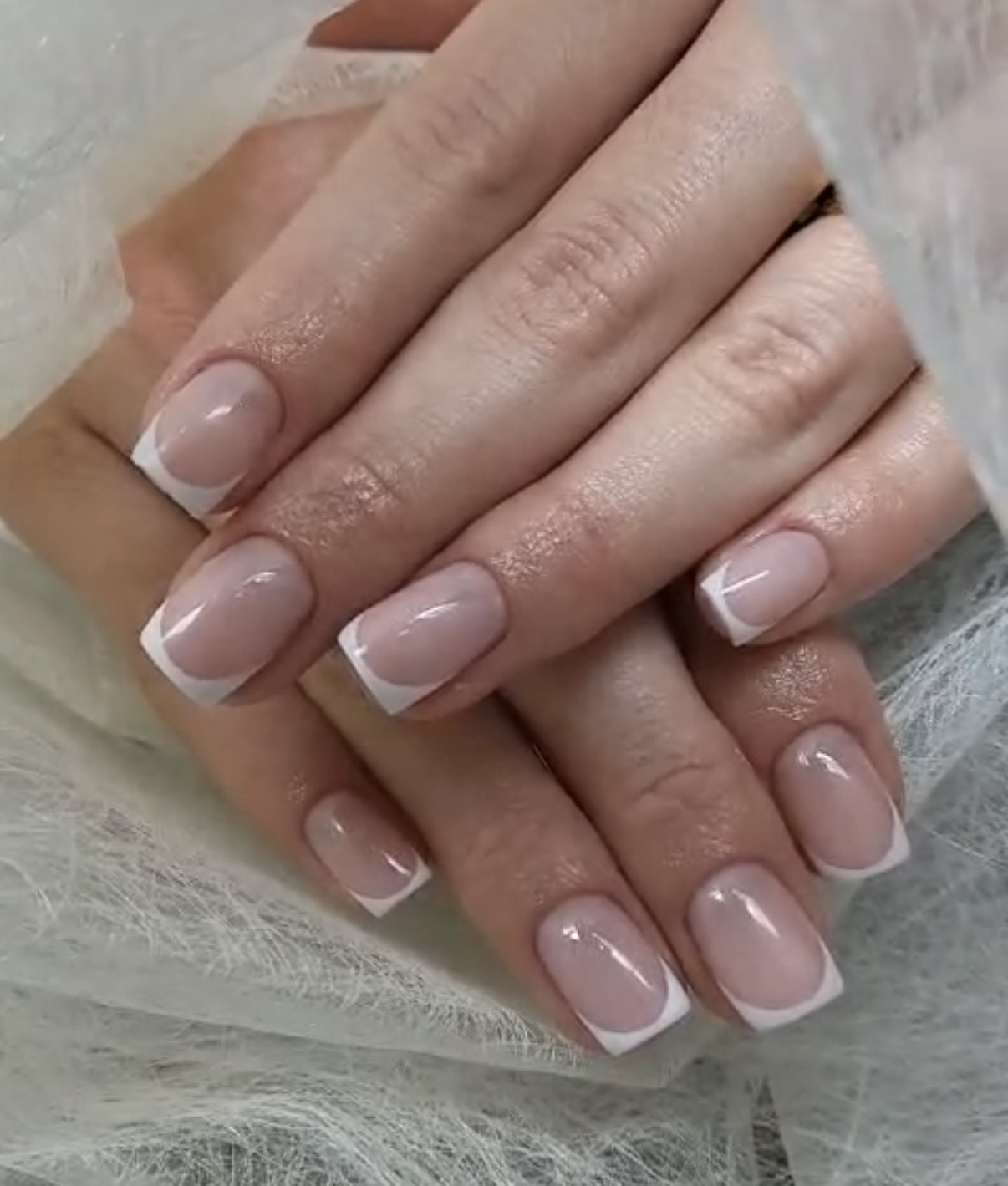 Naturel French manicure met korte vierkante nagels, handen op een witte vacht
